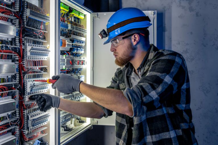 Male electrician working in switchboard with electrical connecting cable. Electrical engineer in special clothes with flashlight on helmet in dark room with emergency lights. Space for text. SSUCv3H4sIAAAAAAAAA41Py46DMAz8F5+DBIUtLL9S9RASA1EDQYmzVYXy7+tQqr1uTvaMM48djIYe6rFsq0aVhS5VV1QVjsXwXcpCtU2DXd2pq9IgQEtC6Ku67qpLXX9dumvblvwEDDIYBf0OxtoYyEsyboWeGY+rRn+MqA05b6TlLQkIJCkGDPyNN8XaE7PH/tG77RnngGwe4pCHJP6J3QXICVf1yvopB7EoD7sbU48noV9Ob0dzjsgiLq7kX28h69wmB8uNR2kDCphlCHygT4A/bt4os05nAy7ulve8OspORx5y6mH0afUuPRtGs88OcbNOatQnHYfFEH1Wjz8Gn3/XKaVfiV598rIBAAA=